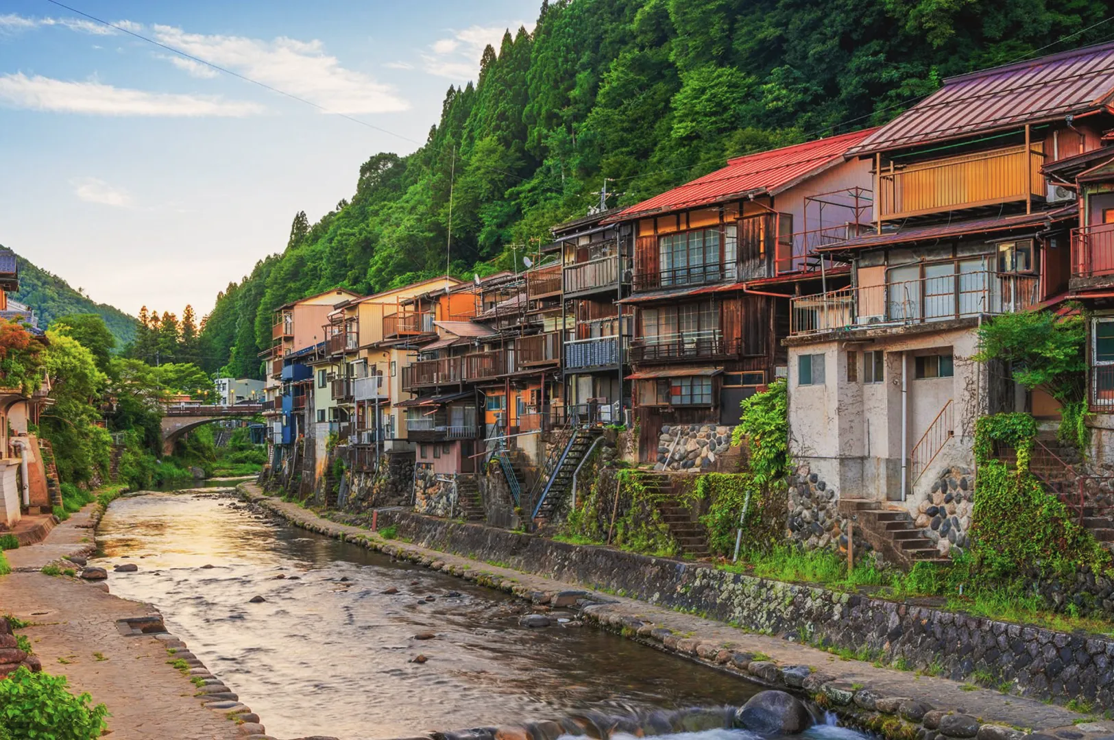 Traditional Japanese wooden buildings along the Yoshida River in Gujo Hachiman, framed by lush forested hills.