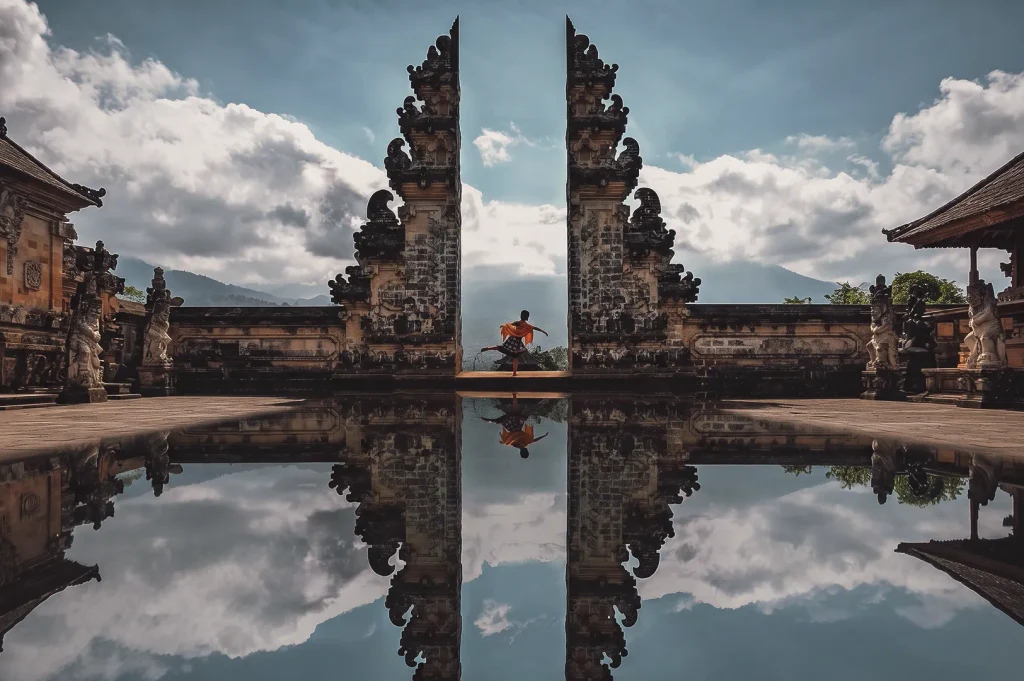 Traditional dancer posing between the stone Gates of Heaven at Pura Lempuyang temple with sky reflection in Bali