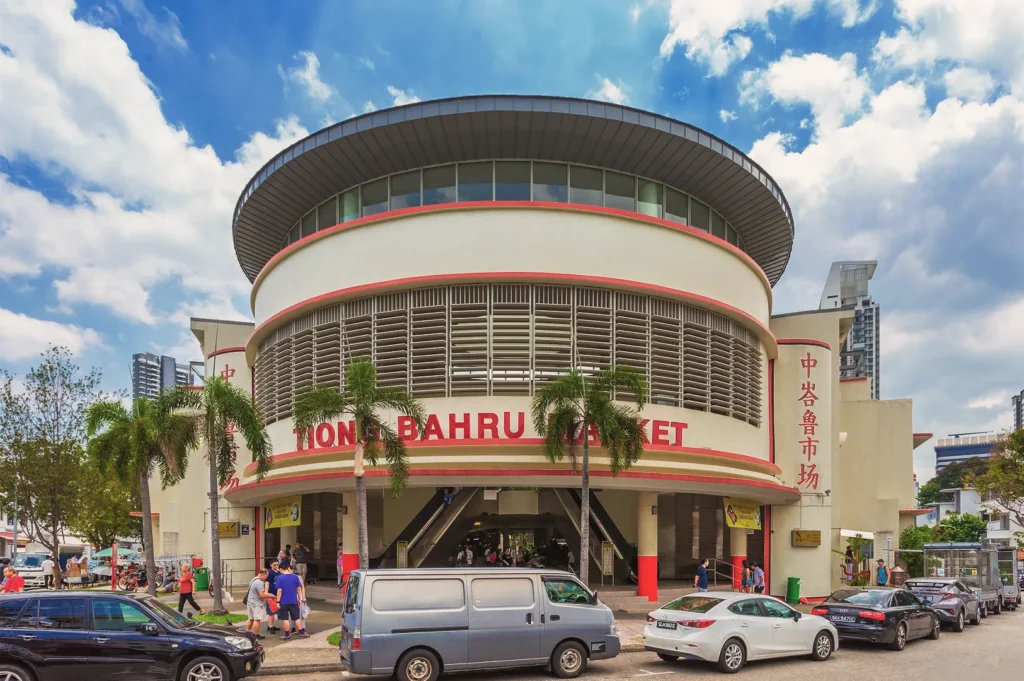 Exterior of Tiong Bahru Market in Singapore featuring its distinctive circular Art Deco design, palm trees, and busy street scene — popular hawker center and local landmark.