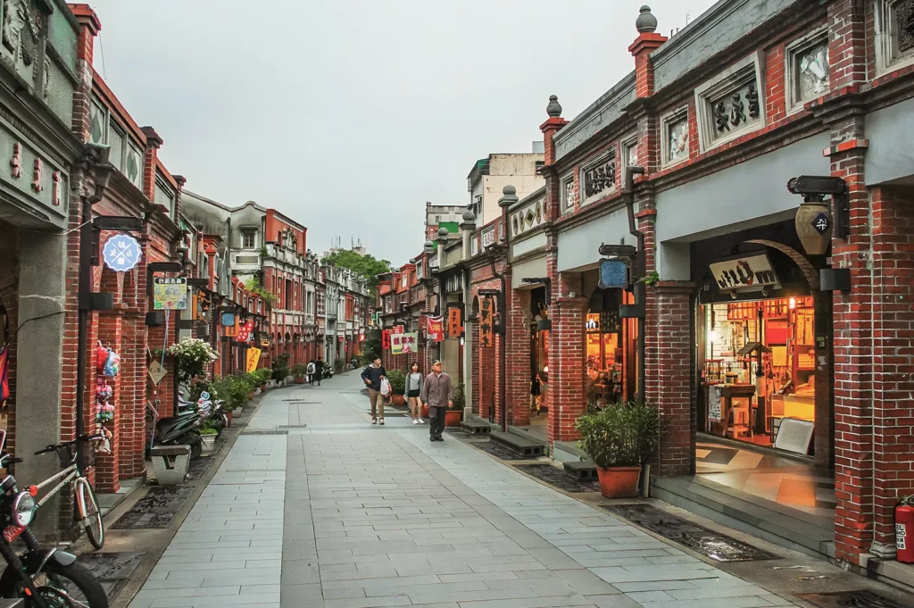 Pedestrian street in Taipei lined with red‑brick heritage buildings and traditional shops, featuring Chinese signage, warm lights, and local architecture.