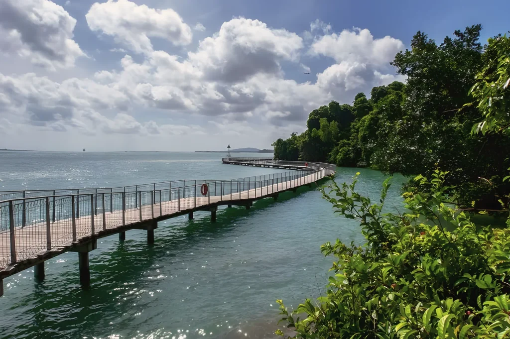 Coastal boardwalk at Chek Jawa Wetlands on Pulau Ubin, Singapore — scenic walkway over turquoise waters surrounded by lush greenery and blue skies.