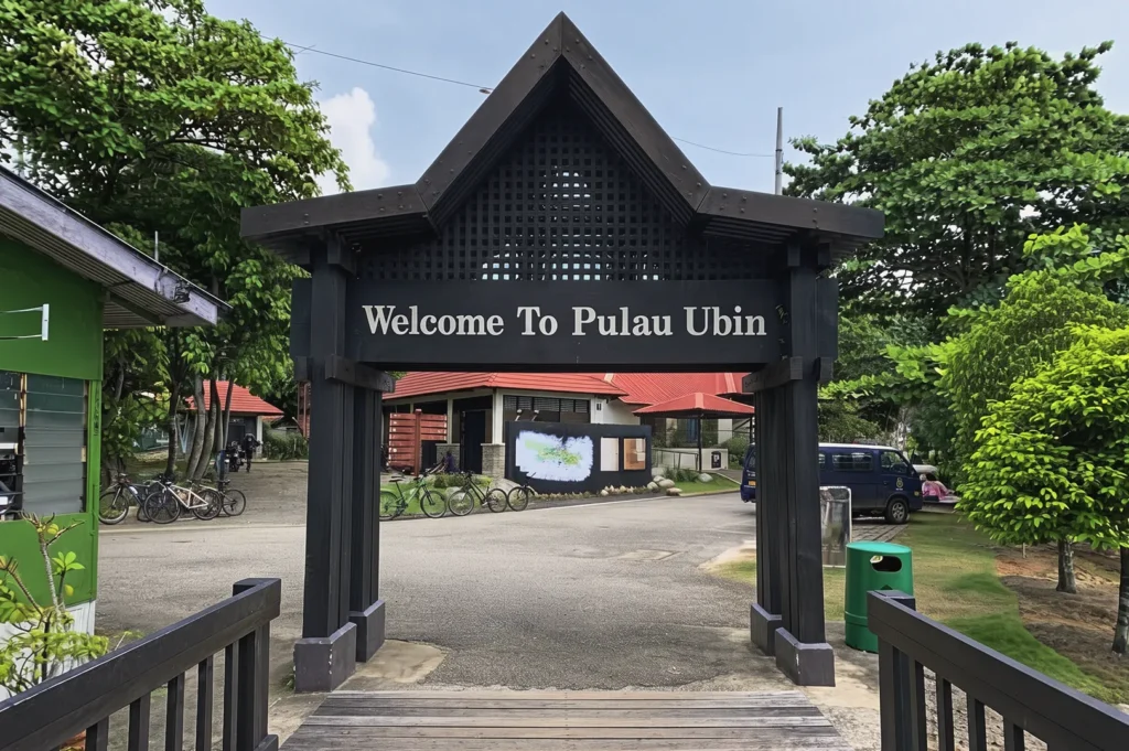 Entrance gate reading “Welcome to Pulau Ubin” surrounded by tropical greenery and rustic buildings — scenic island getaway in Singapore known for cycling and nature trails.