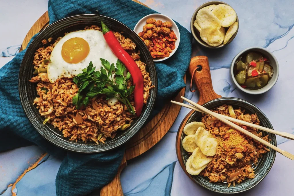 Authentic Indonesian Nasi Goreng fried rice topped with a fried egg, fresh parsley, and red chili pepper served with side condiments