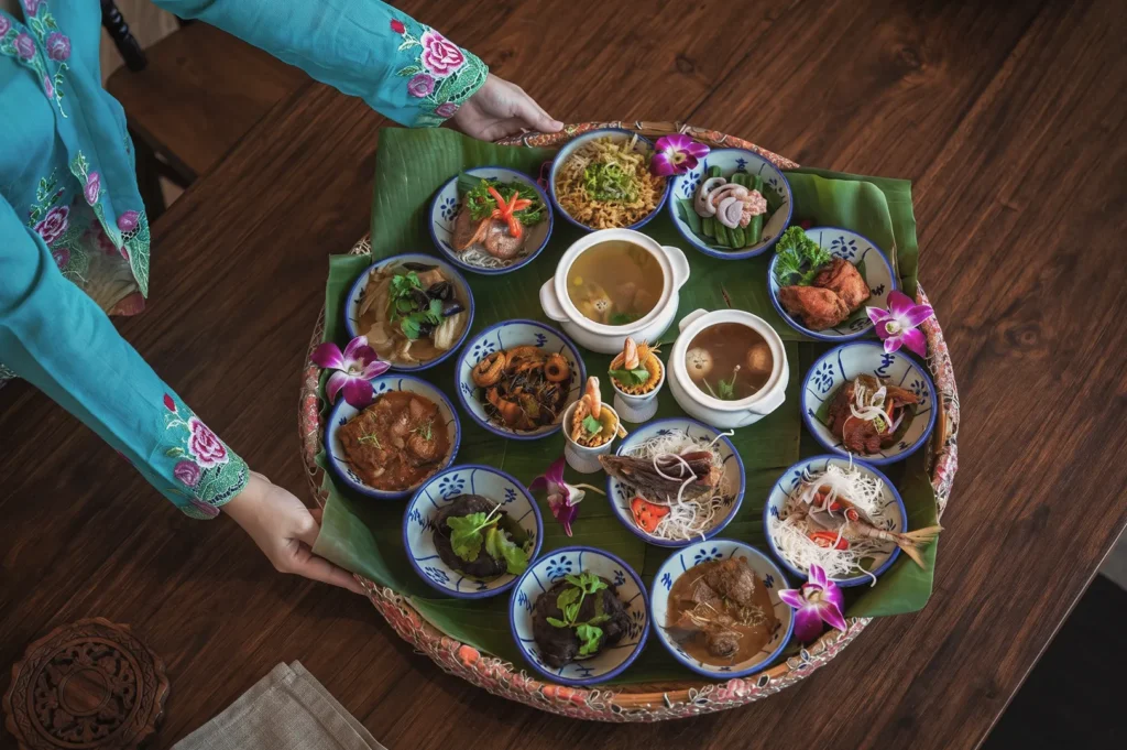 Traditional Peranakan meal served in blue patterned bowls on banana leaves — authentic Singaporean cuisine with floral garnishes and cultural presentation.