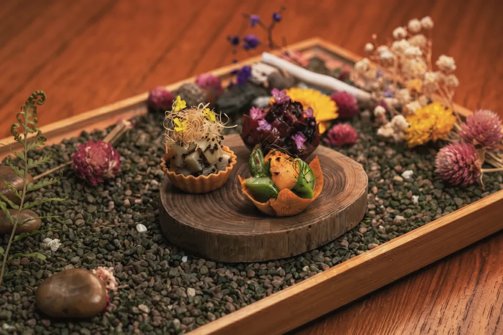 Artistic fine‑dining presentation of bite‑sized dishes with edible flowers and natural décor — creative Singapore restaurant plating inspired by nature.