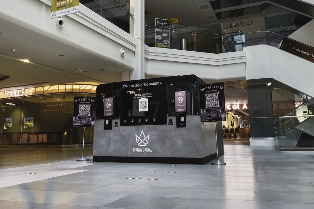 Modern automated coffee kiosk by Crown Digital featuring “Ella the Robotic Barista” in a shopping mall, showcasing innovation in smart café technology and contactless service.