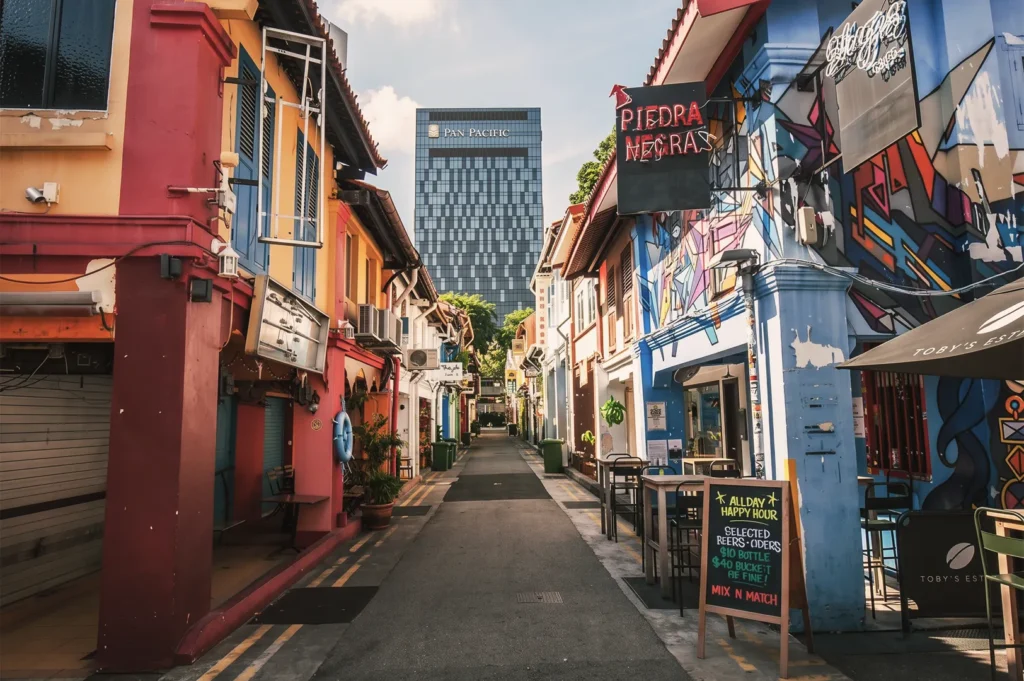 Vibrant street scene at Haji Lane Singapore featuring colorful shophouses, street art, and cafés with the Pan Pacific Hotel tower in the background, highlighting the city’s blend of heritage and modern architecture.