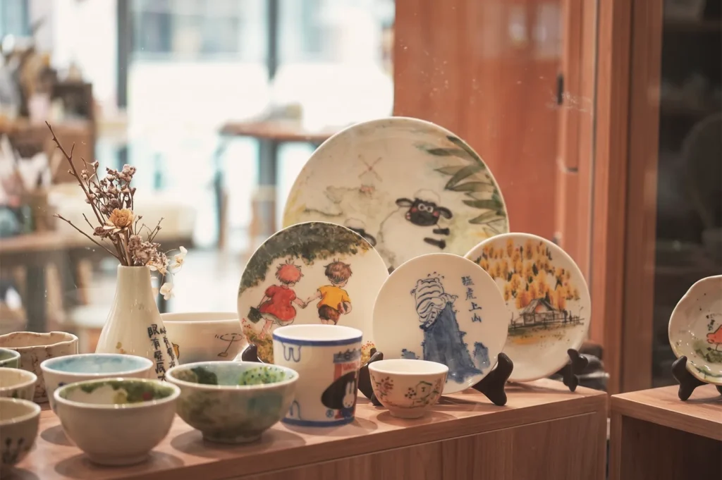 Close‑up of hand‑painted ceramic plates and bowls at Taoz Ceramics Studio featuring whimsical designs and Chinese calligraphy — artisanal pottery collection in Singapore.