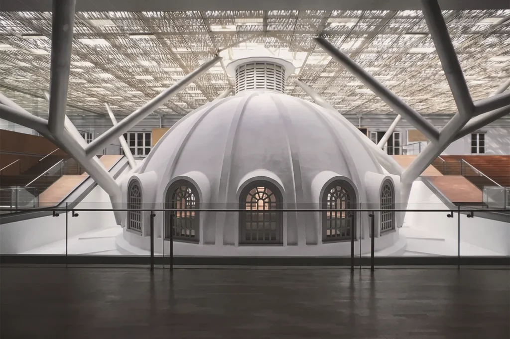 Modern architectural integration featuring a white dome with arched windows beneath a patterned skylight supported by steel beams.