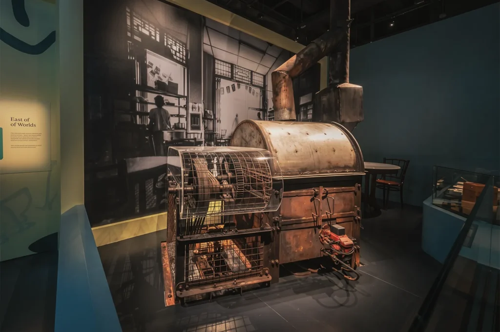 Vintage industrial machine displayed in a museum setting with historical photographs and interpretive panels highlighting Singapore’s heritage.