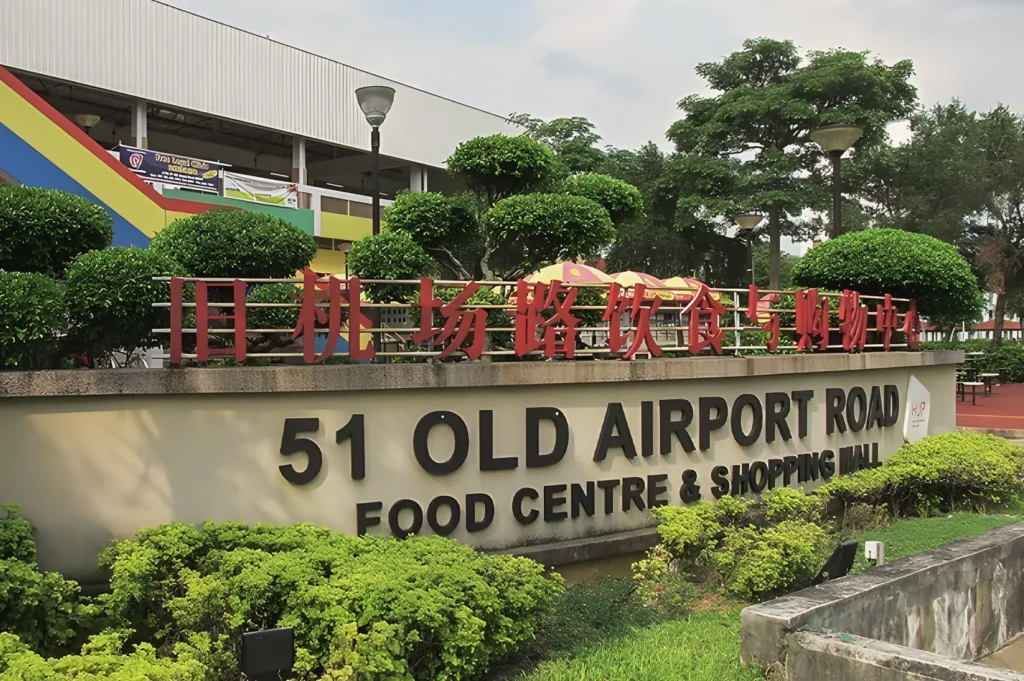 Entrance sign of 51 Old Airport Road Food Centre Singapore with bilingual text and lush greenery surrounding the iconic hawker landmark.